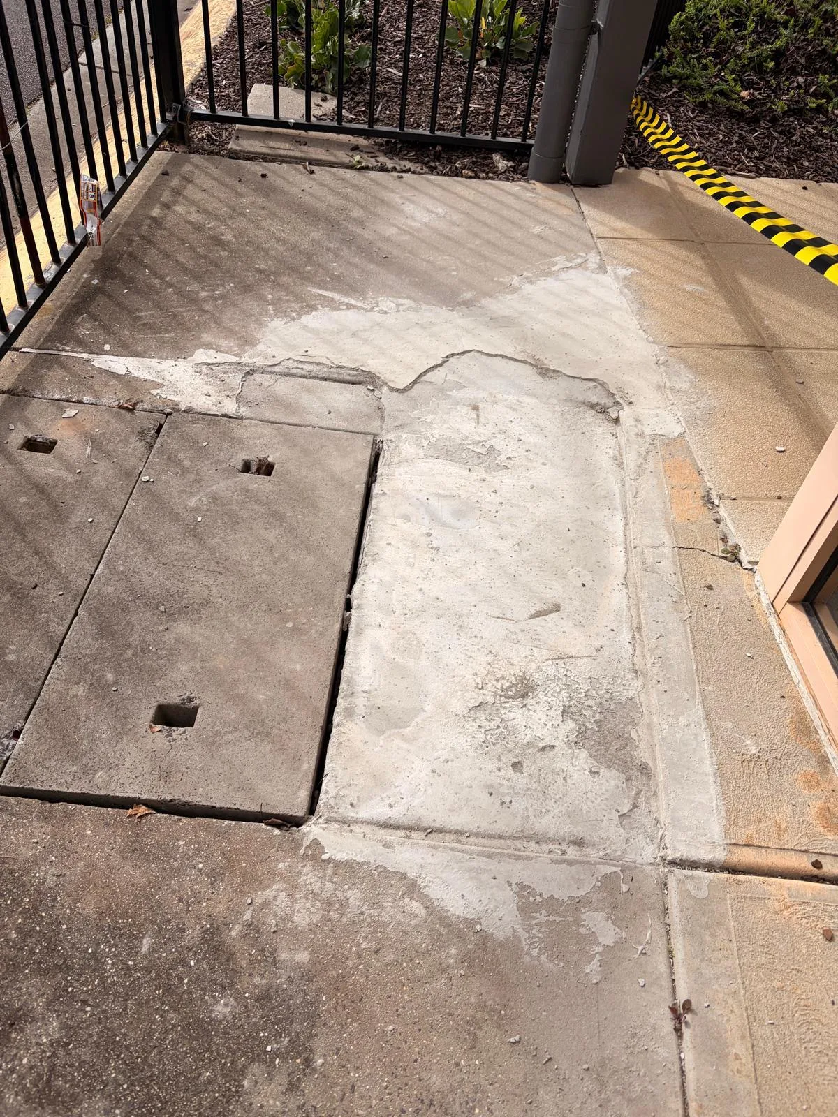 Failed concrete path with rough patch repairs around the pit lids before breakout